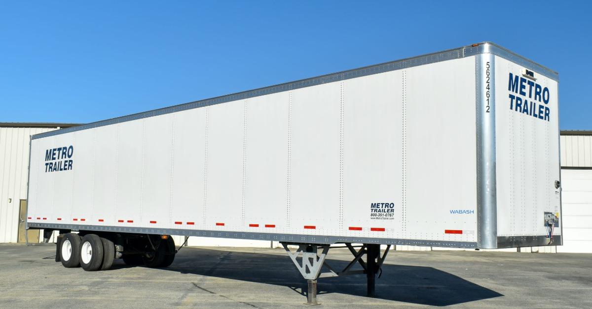 A close-up of a commercial enclosed trailer parked in an empty area of a parking lot near a large building.
