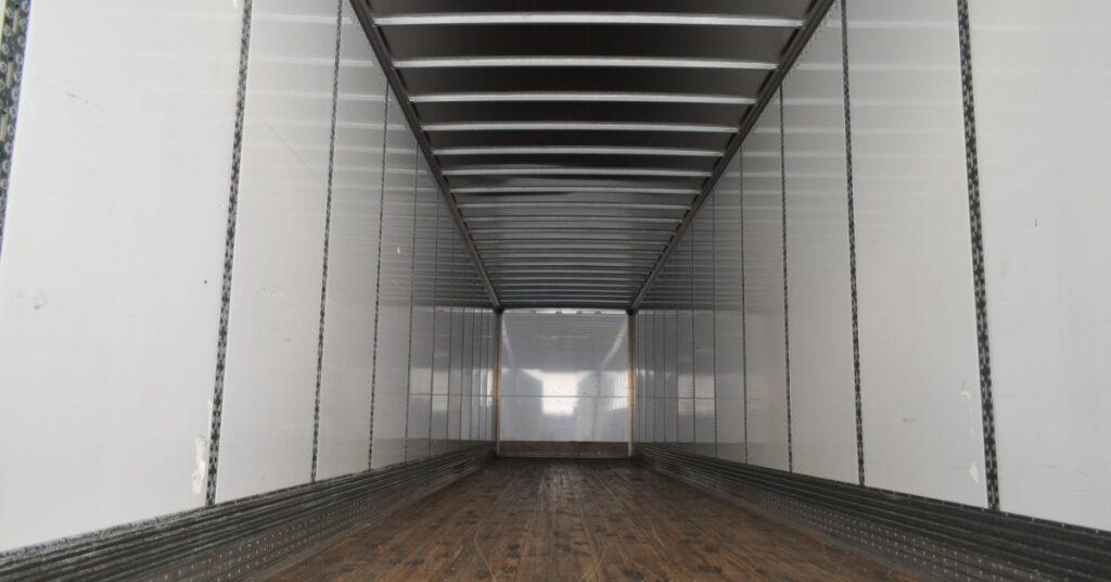 A close-up of the interior of a commercial enclosed trailer. The walls are white with silver supports.