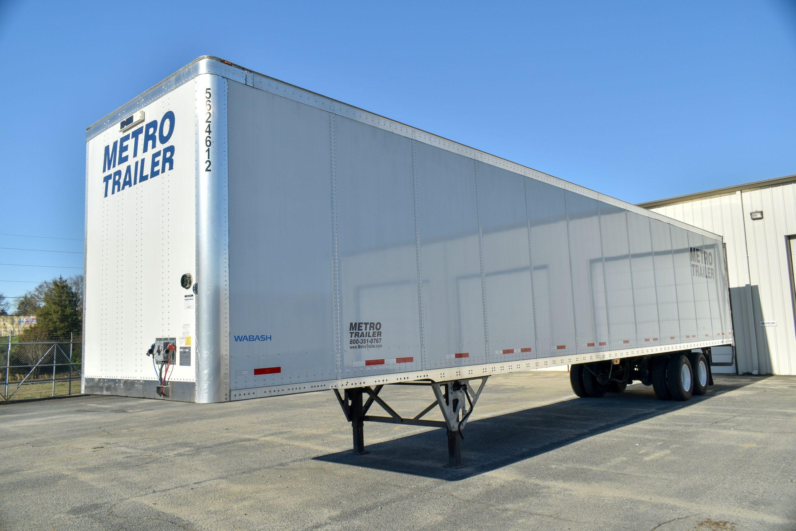 A large white Metro Trailer semi-trailer parked on pavement outside a warehouse under a clear blue sky.
