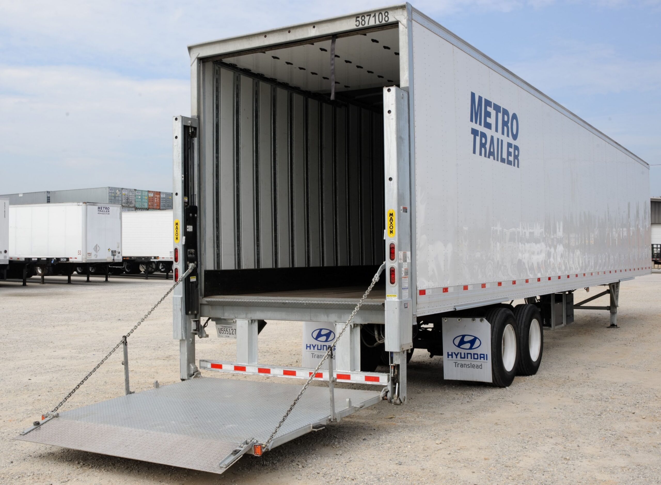 A large Metro Trailer semi-trailer with its rear open and a liftgate lowered onto a gravel parking lot.